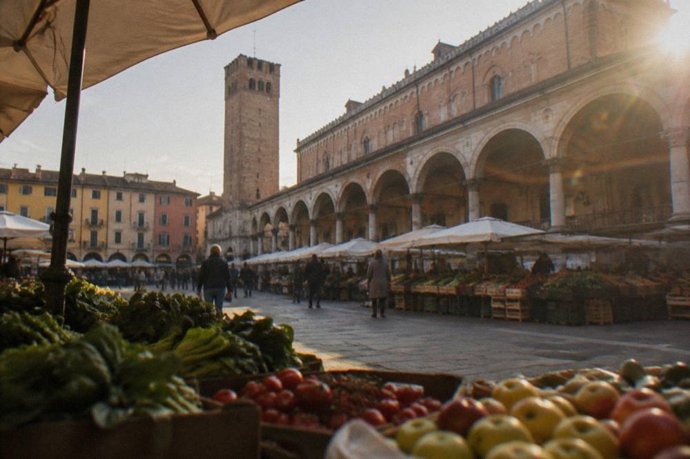 Piazza delle Erbe in Padua with market stalls set out beneath the arcades and the tower of Palazzo della Ragione behind