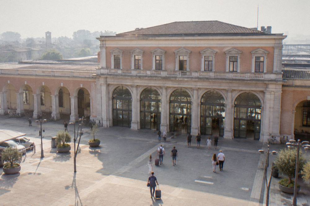 The facade of Padua train station seen from the forecourt with travellers walking toward the entrance