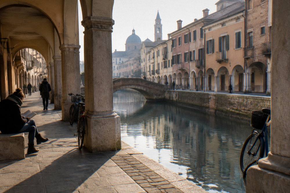 Travellers reading a map beside an arcaded street in Padua at dusk