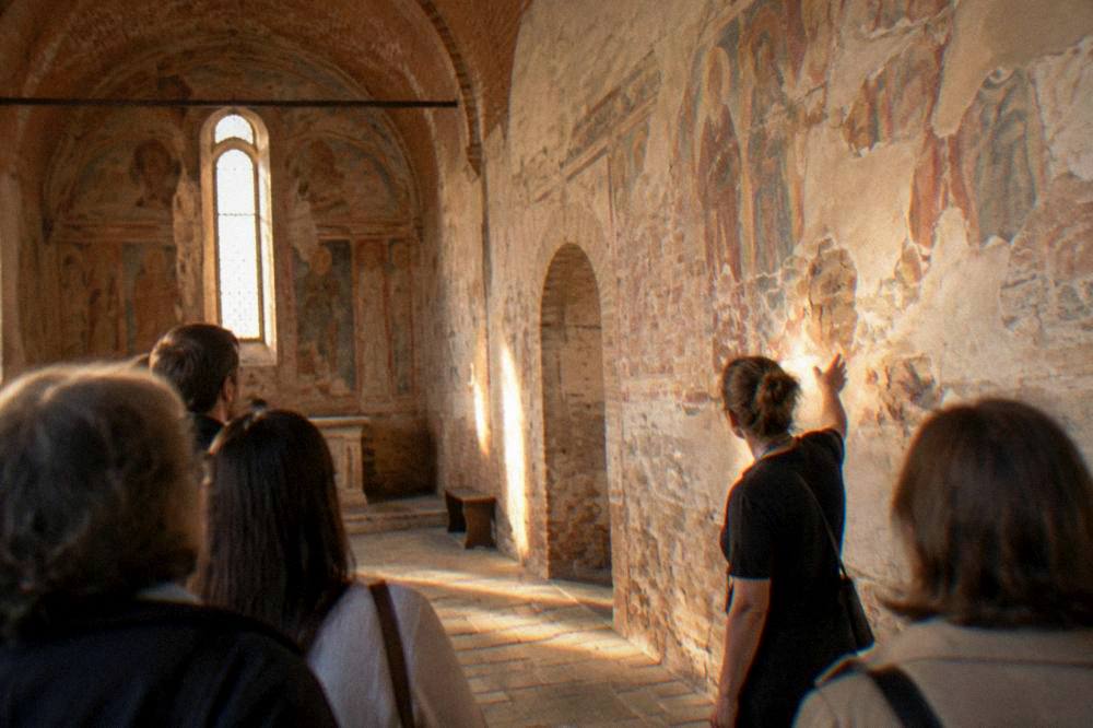 A guide pointing at frescoes while a small group listens inside a chapel