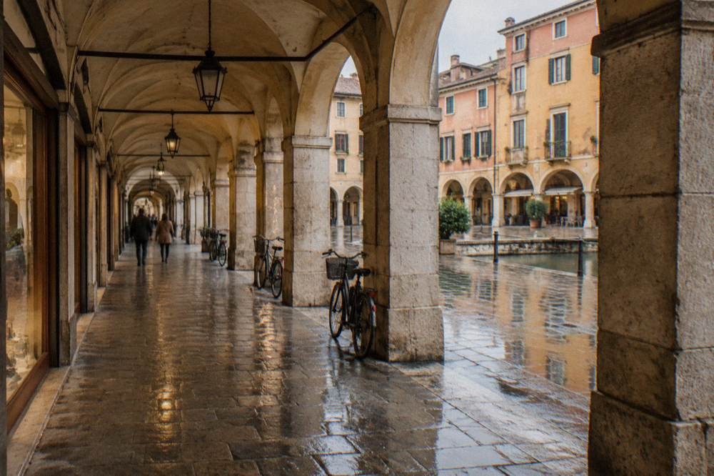 Covered arcade in Padua with stone vaults and shopfronts during light rain