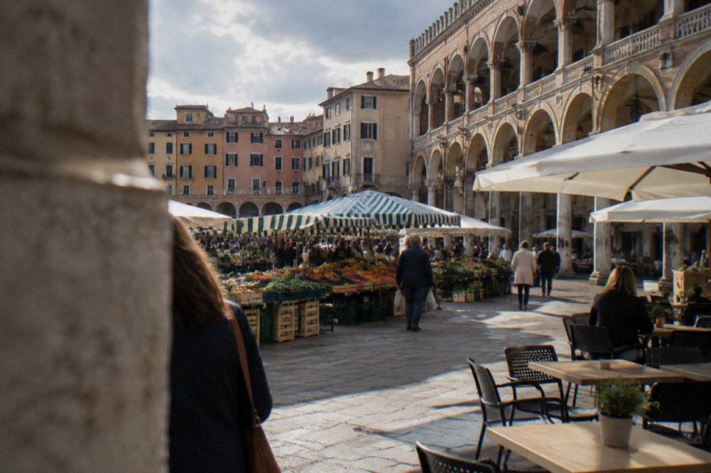 An arcaded Italian market square with striped stalls and café tables
