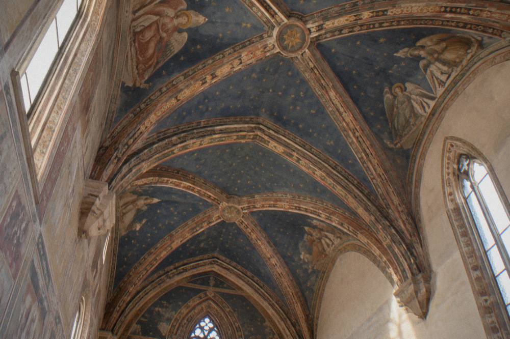 A frescoed vault ceiling with star patterns seen from below inside a chapel
