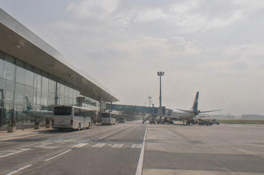A small regional airport terminal with a single aircraft at the gate and a low building under a cloudy sky