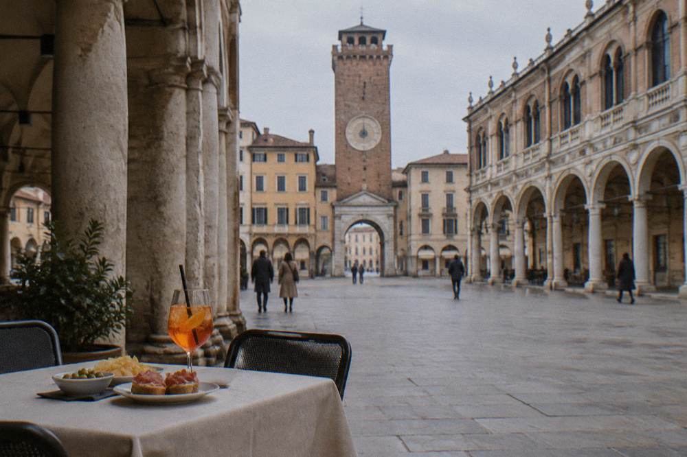 A covered table with a glass of spritz and small plates under the porticoes near Piazza dei Signori in Padua