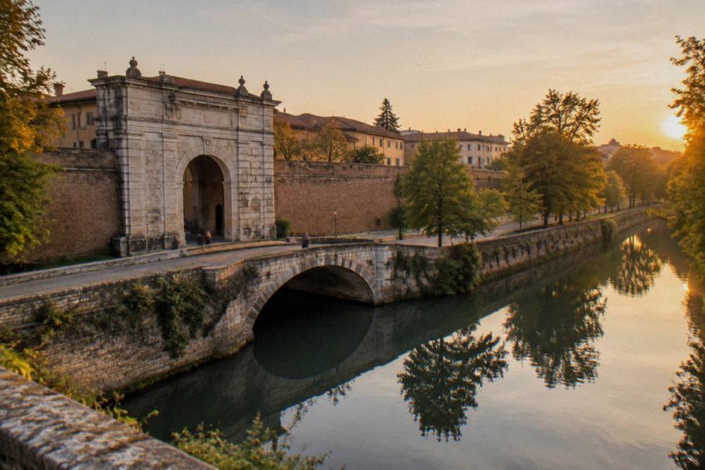 A quiet canal along the city walls near Porta Portello in Padua with trees reflected in the water