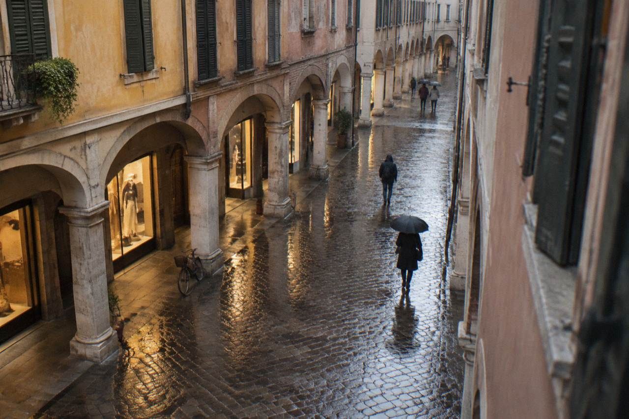 Rainy arcade street in Padua with wet cobblestones reflecting the lights of shop windows