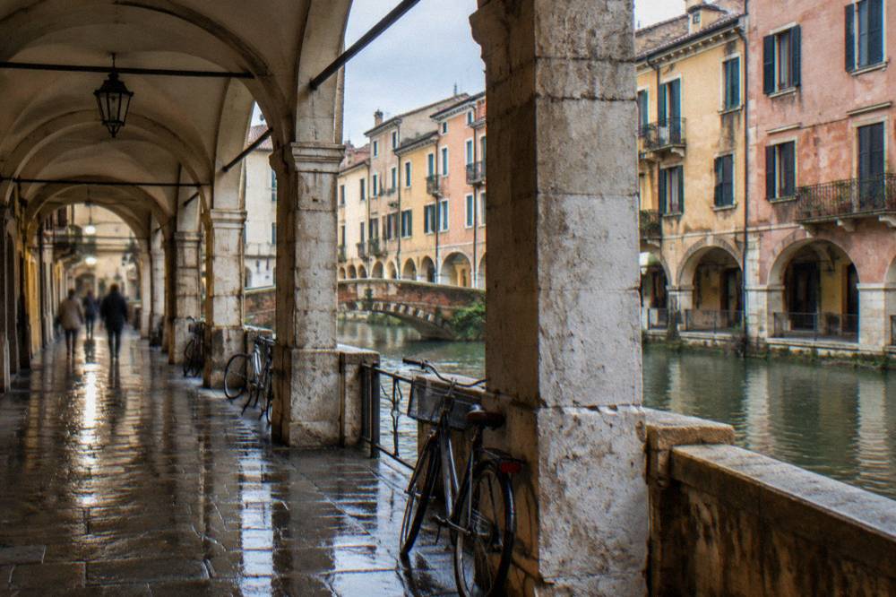 Stone arcade with arches over a Padua sidewalk during light rain