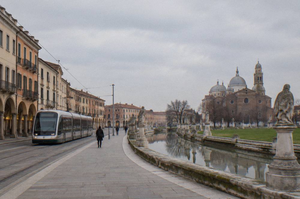 Modern tram passing historic arcaded buildings on a city street