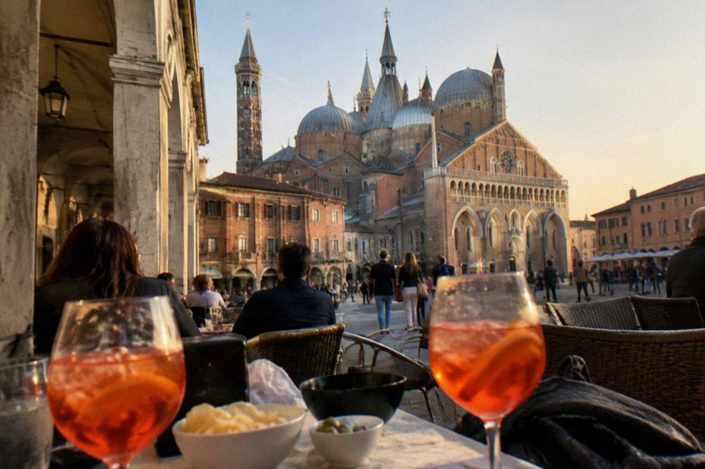 Evening crowd with spritz glasses at outdoor tables in an arcaded piazza