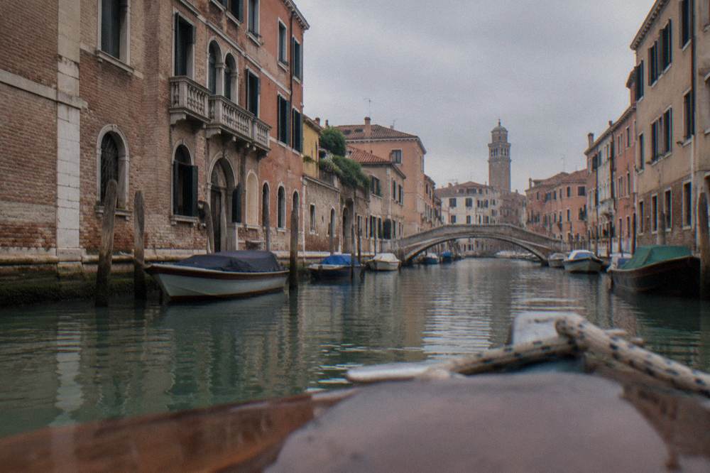 Canal with moored boats and old brick buildings in Venice seen from the water