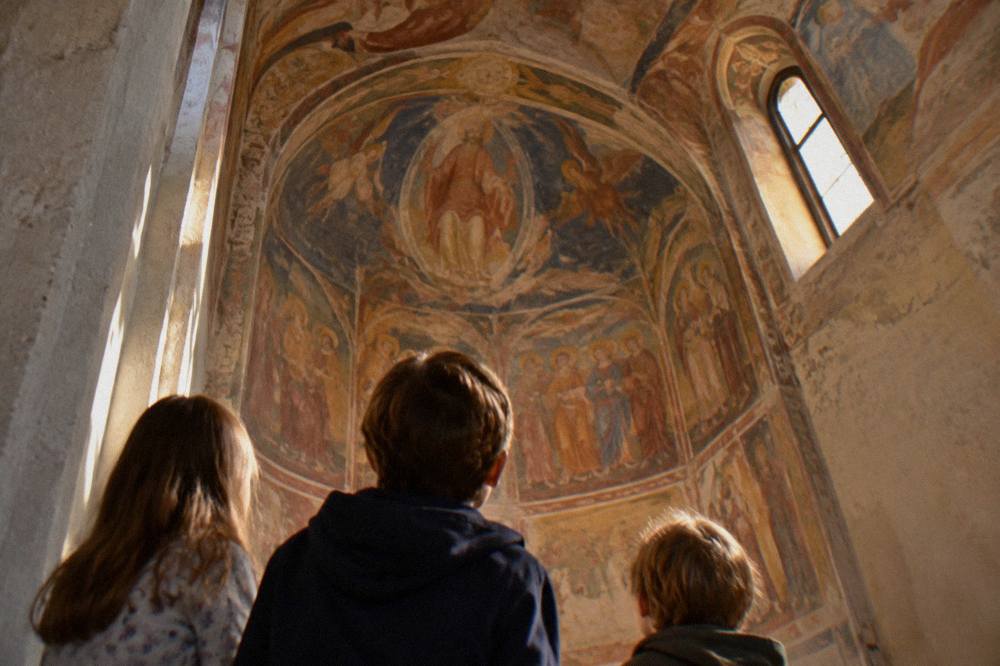 Children looking up at the colorful frescoed walls inside a small chapel