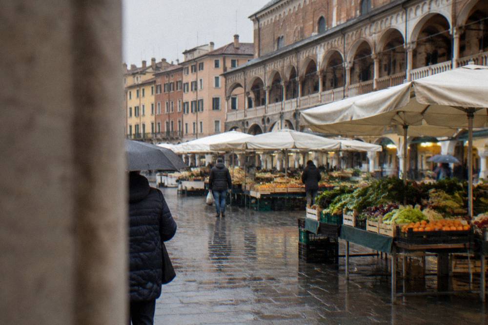 A market square in Padua with fruit and vegetable stalls under white awnings