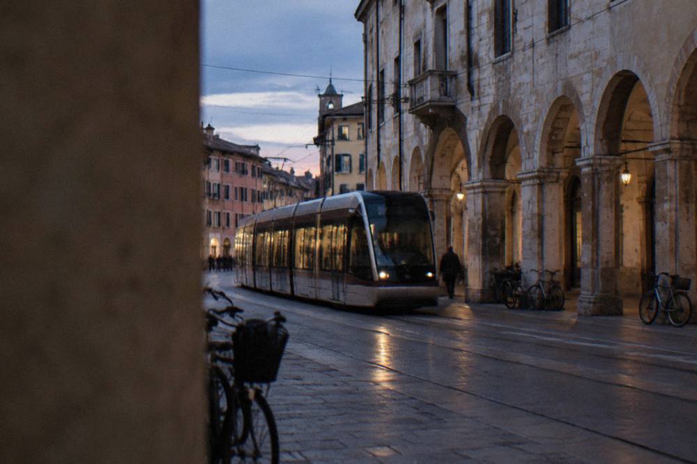 A modern tram passing an old stone building on a Padua street