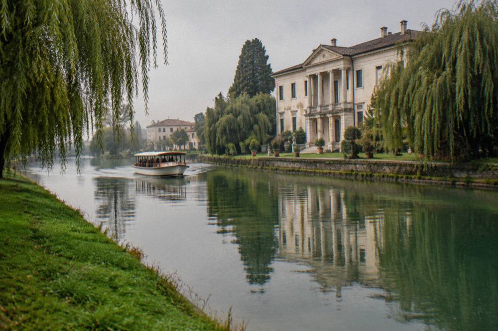 A historic Venetian villa with a pale facade reflected in the water of the Brenta canal
