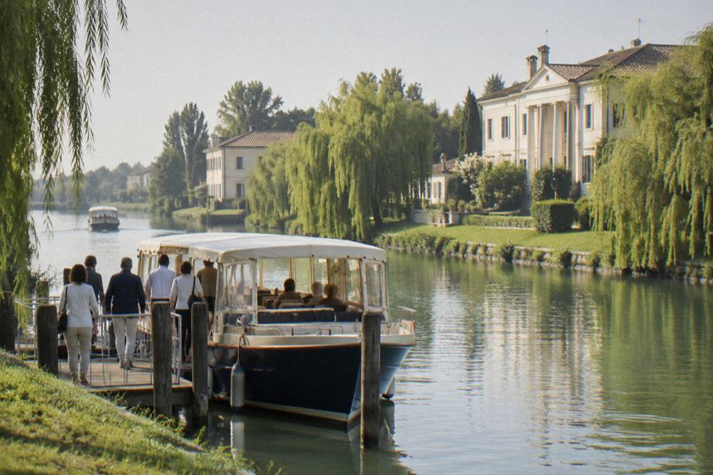 Passengers boarding a small cruise boat at a jetty on a canal in northern Italy