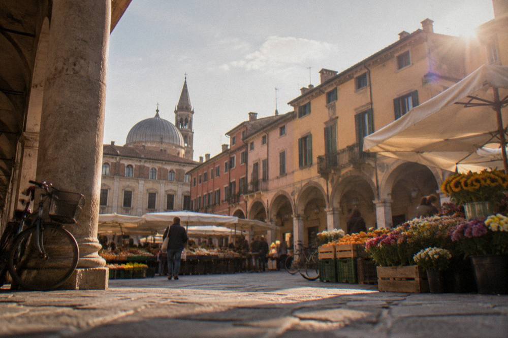 Market stalls with fruit and flowers filling a Padua square beside old arcaded buildings