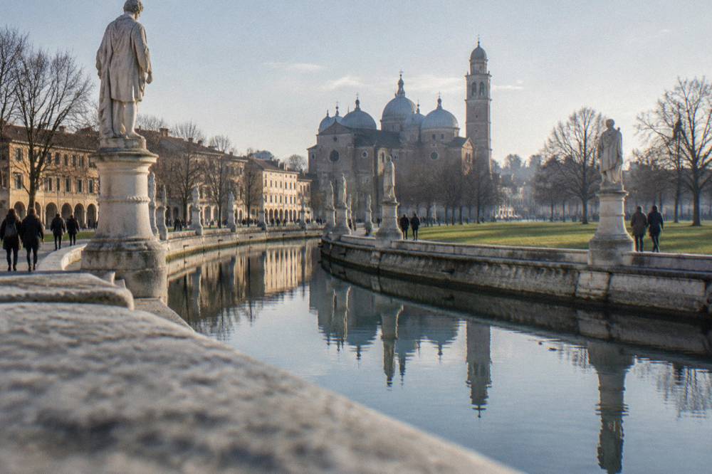 Visitors walking beside the canal and statues ringing Prato della Valle